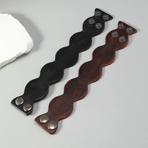 Close-up of retro wave-edge leather bracelets in black and brown with snap buttons