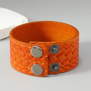 Close-up of wide orange leather bracelet with woven embossed texture and metal snaps