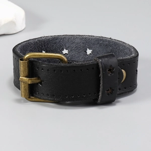 Détail du bracelet large en cuir noir avec étoiles ajourées et boucle en bronze