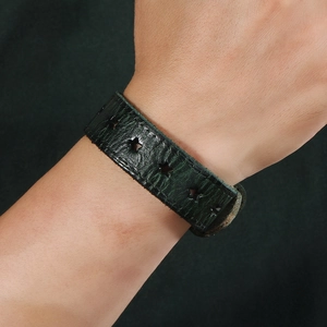Détail d'un bracelet en cuir vert foncé avec des étoiles ajourées porté au poignet
