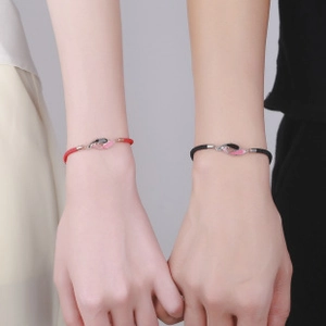 Close-up of red and black woven bracelets with interlocking silver carp fish charms