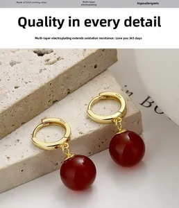 Detail of gold-plated 925 silver hoop earrings with deep red agate spherical pendants