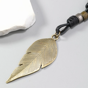 Detail of vintage bronze feather pendant with textured leather cord and metallic beads