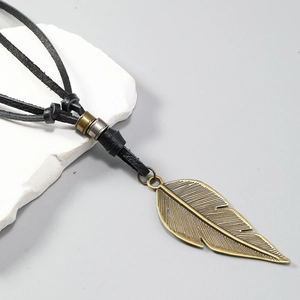 Close-up of bronze feather pendant with detailed texture on a black leather cord necklace