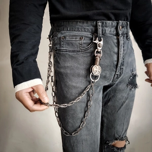 Detail of multi-layered punk metal pant chains with gothic cross charm on grey jeans