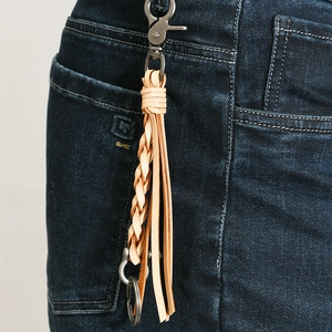 Detail of hand-woven leather tassel keychain on blue denim showing vintage metal clasp