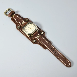 Detail view of brown leather cuff watch with punk rivets and contrast white stitching