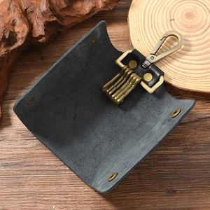 Vintage black leather key case with brass hooks on dark wood background