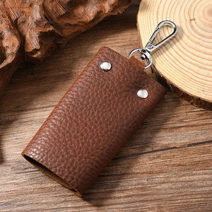 Detail of dark brown leather key case with silver snap buttons on a rustic wood background
