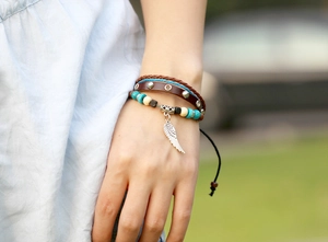Dettaglio del bracciale in pelle multistrato con ciondolo a piuma d'argento e perline boho