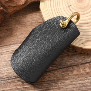 Detail of lychee pattern leather key case with vintage brass D-ring on wood background