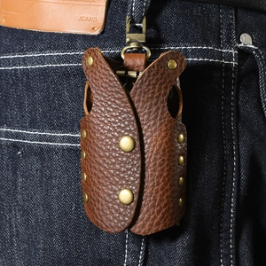 Vintage brown lychee grain leather vest-shaped key case with rivets on blue denim jeans