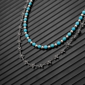 Detail of layered turquoise beaded chain with silver engraved star pendants on black background