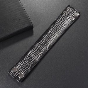 Detail of wide black leather punk bracelet with distressed zebra pattern and metal snaps