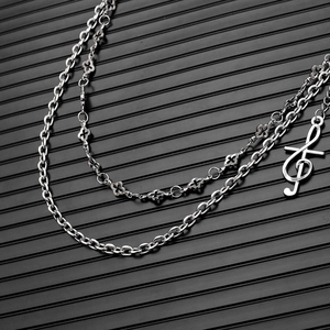 Détail macro d'une chaîne argentée à double couche avec pendentif clé de sol et trèfle