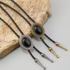 Vintage western bolo tie with black stone pendant and woven leather cord on a rock base