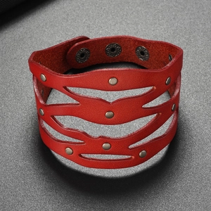 Détail macro du bracelet en cuir rouge ajouré avec des rivets métalliques et pressions