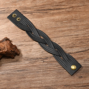 Detail of woven black leather bracelet featuring golden metal snap buttons on wood