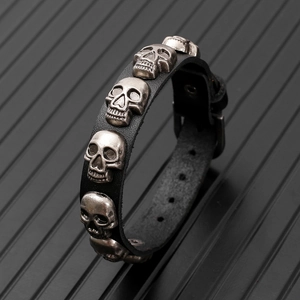 Detail of adjustable black leather punk bracelet featuring multiple silver skull charms