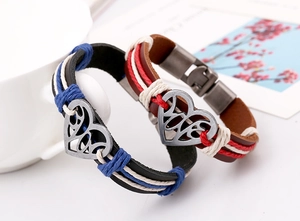 Dettaglio macro di braccialetti in pelle intrecciata con ciondolo a cuore e chiusura in metallo