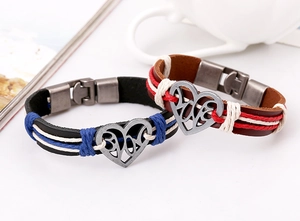 Dettaglio dei bracciali di coppia in pelle intrecciata con ciondolo a cuore in metallo