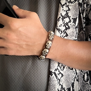 Detail of retro punk leather bracelet featuring four vintage silver skull ornaments