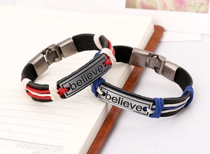 Detail of braided leather bracelets with engraved believe metal plate on a notebook