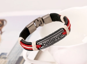 Detailed close-up of woven leather bracelet with metal plate engraved with Believe