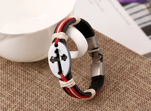 Close-up of a woven leather bracelet featuring a cross-engraved oval metal pendant