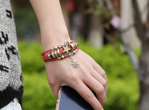 Detail of red multilayer leather bracelet with snowflake charm and metallic star beads