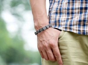 Detail of a punk leather bracelet with silver cross charms worn in a casual setting