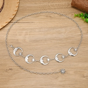 Detail of silver chain belt featuring hollow moon and sun starburst charms on wood surface