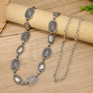 Retro silver metal waist chain with etched patterns on a minimalist fabric roll background