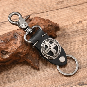Detail of punk style leather keychain with bronze cross and fish emblem on wood background