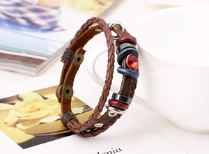 Dettaglio di bracciale multistrato in pelle vintage con gemma rossa su tazza da caffè
