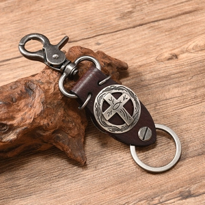 Detail of vintage punk leather keychain with cross pendant on a rustic wood background