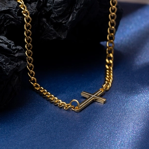 Gold-plated Cuban link necklace with horizontal cross pendant on textured backdrop