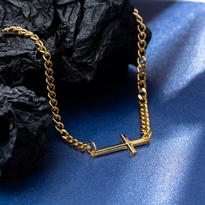 Detailed view of golden lateral cross necklace with polished curb chain on a dark background