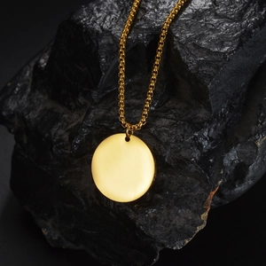 Minimalist gold titanium necklace with smooth round pendant on a dark stone background