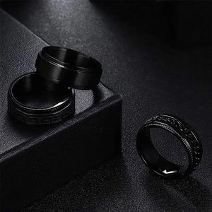 Three men's black titanium rings with Greek key and chain textures on leather display