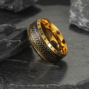 Vintage gold Viking rune ring with black Celtic knot patterns on a rustic rock surface