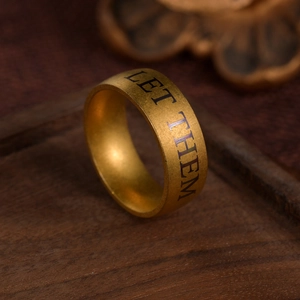 Bague LET THEM en or mat avec gravure vue à 45 degrés sur un support en bois