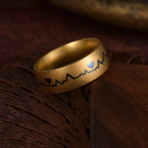Golden matte steel ring with black heartbeat line and blue metallic heart on wood