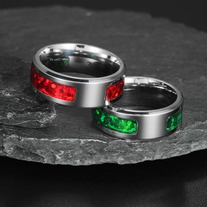 Macro shot of steel rings with sparkling red and green inlay on dark rock base