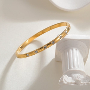 Minimalist gold titanium steel bracelet with embedded cubic zirconia on a white pedestal