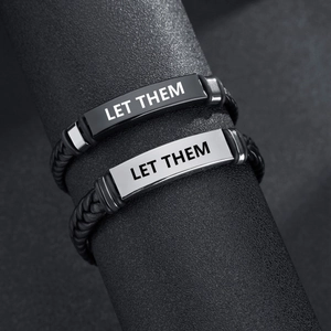 Close-up of woven leather bracelets with engraved metal plates reading LET THEM