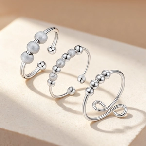 Three silver adjustable fidget rings with rotating beads on a minimalist stone display