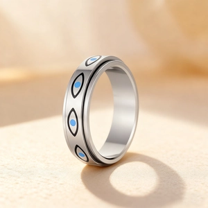 Polished stainless steel spinner ring with blue evil eye charms on a beige textured surface