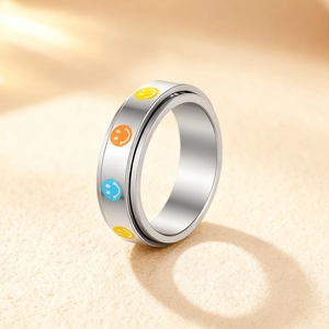 Polished stainless steel spinner ring with colorful smiley faces on sand background