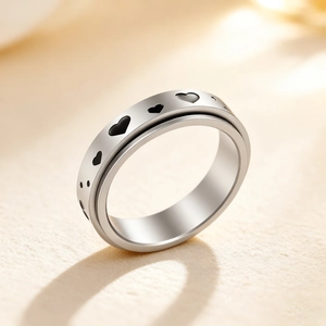 Spinner stress relief ring in stainless steel with black heart patterns on beige surface